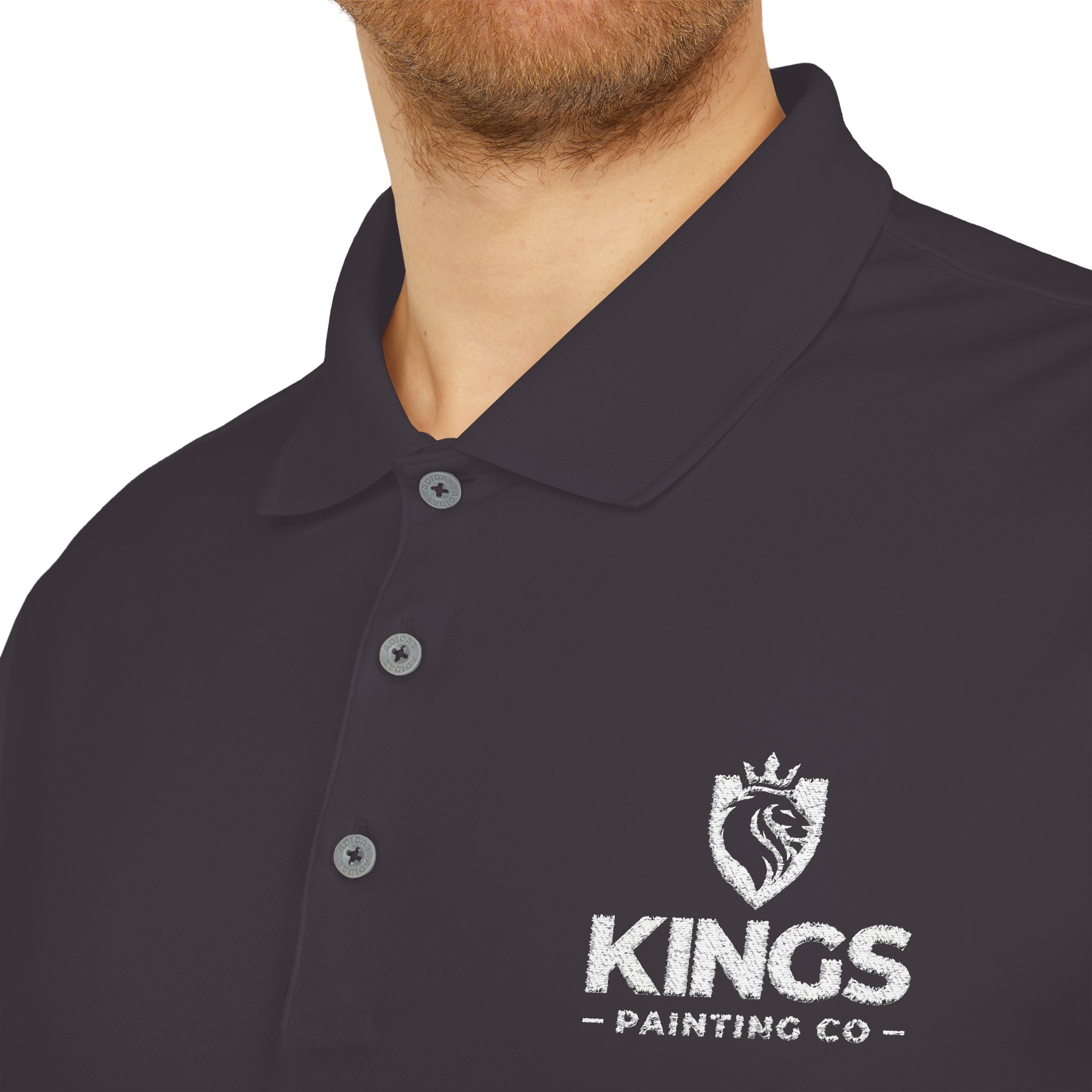 Close-up of a person wearing the Kings Painting Co. Performance Polo by Under Armour®, featuring a white crowned lion’s head logo on the left chest. Only the lower face, neck, and shirt are visible.